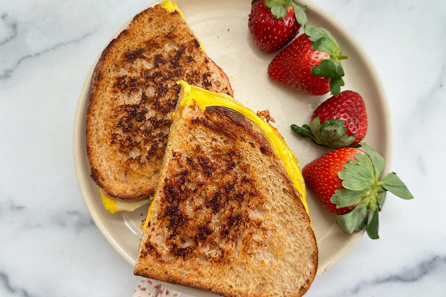 Toasted breakfast sandwich with Canadian bacon and strawberries on the side