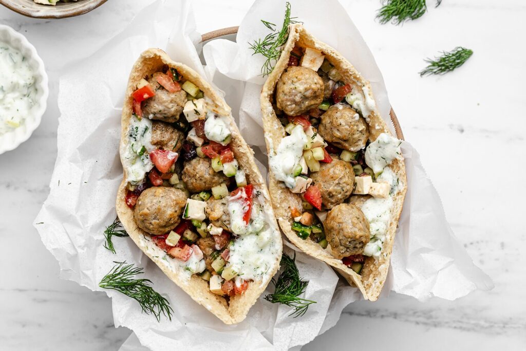 Two pitas filled with chicken meatballs, tomatoes, cucumbers, and tzatziki.