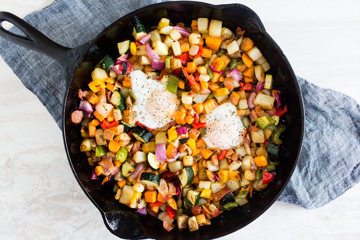 Skillet hash with eggs, bacon, sweet potato, bell peppers, and zucchini.