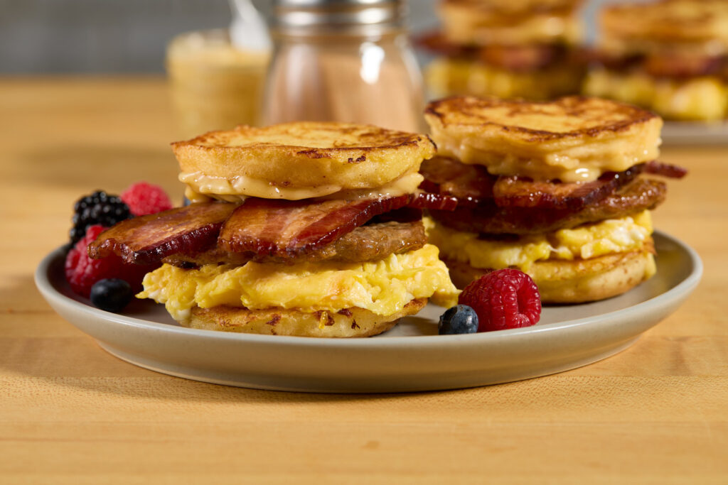 Breakfast sandwiches with eggs, sausage, and bacon on French toast.