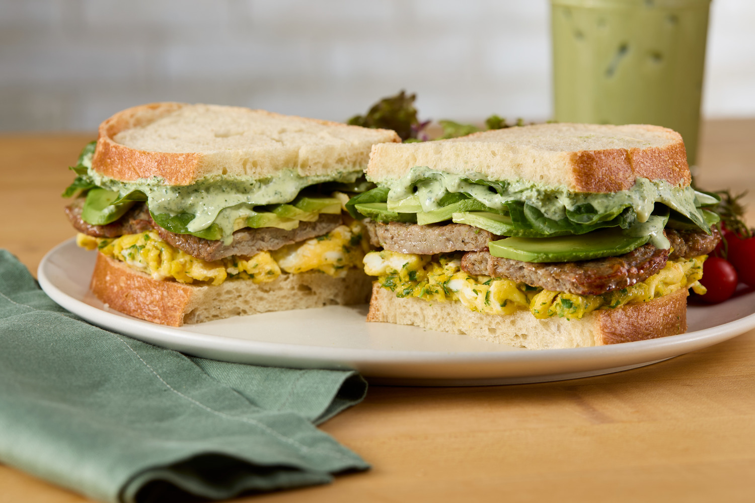 A breakfast sandwich with egg, pork sausage, avocado, and green goddess sauce.