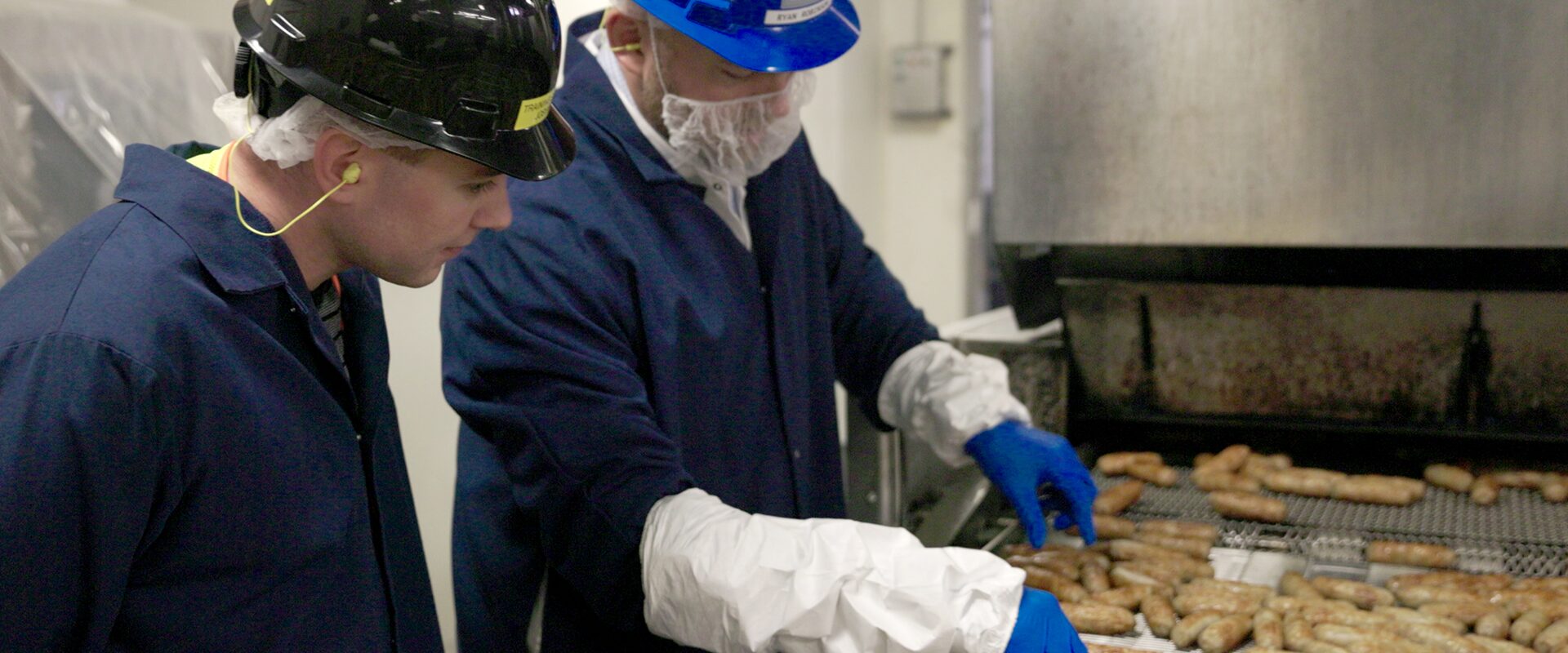 Two employees inspect sausage links.