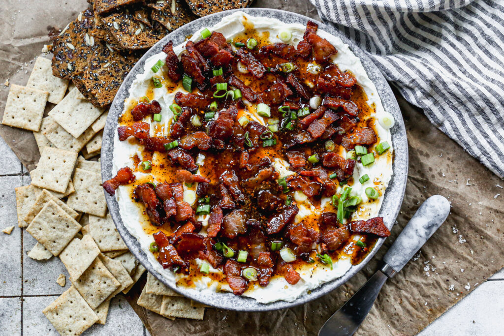 A bowl of whipped brie with bacon dip served with crackers.